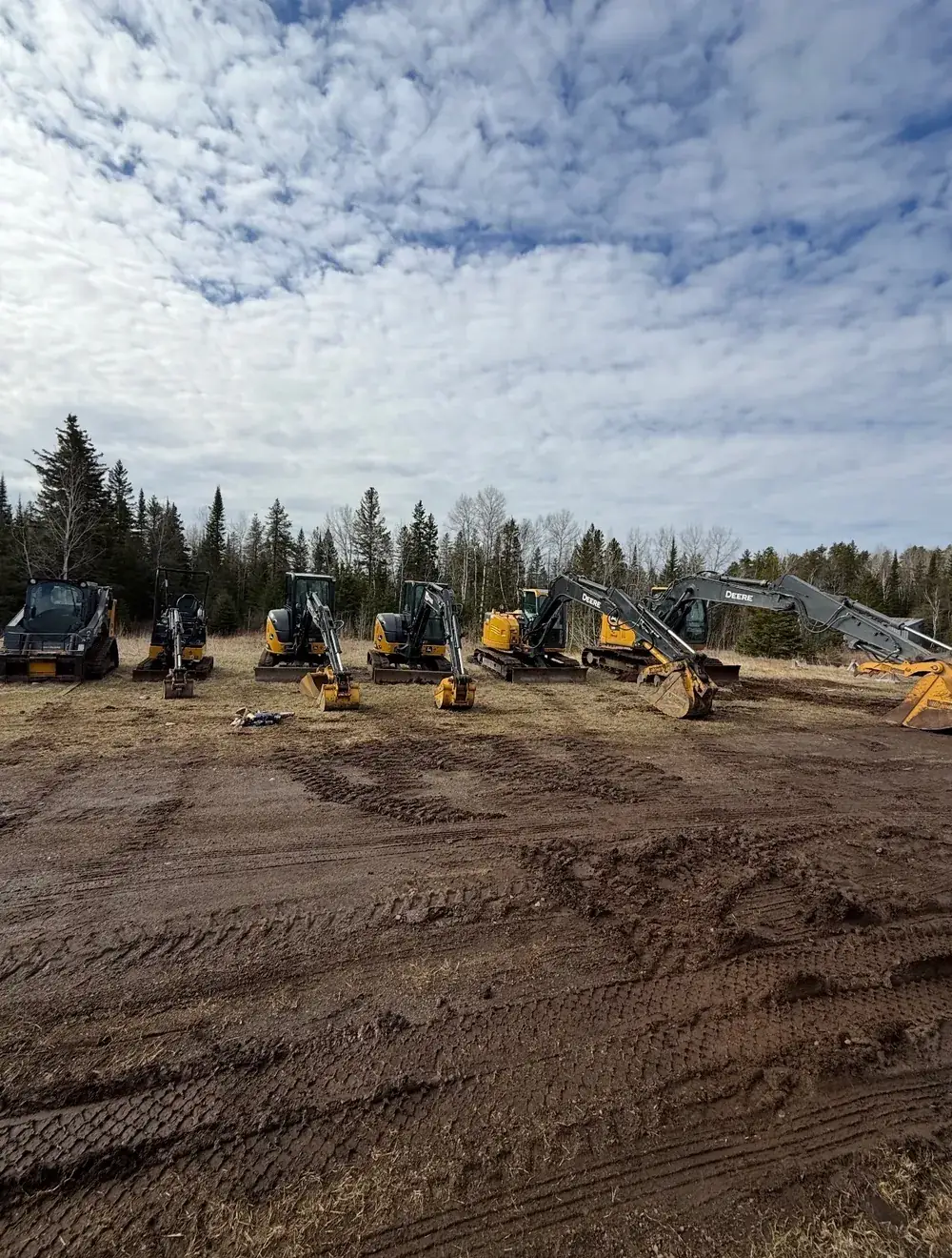 Superior Yard Works John Deere excavators and skid steer lined up in a cleared yard