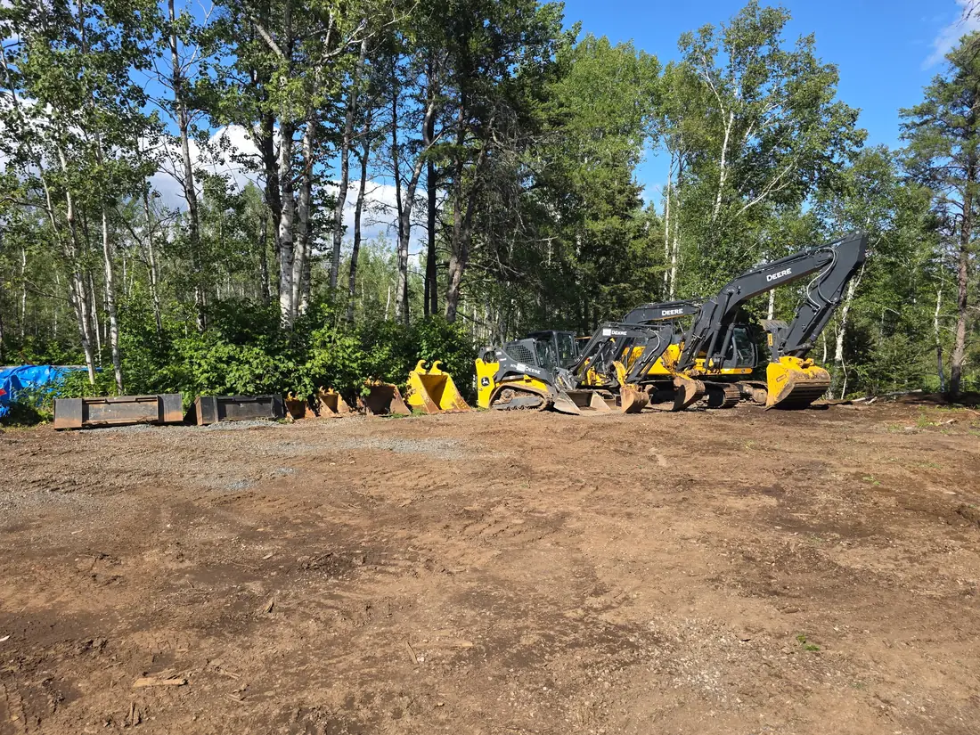 Superior Yard Works John Deere excavators, skid steer and buckets lined up in a cleared yard