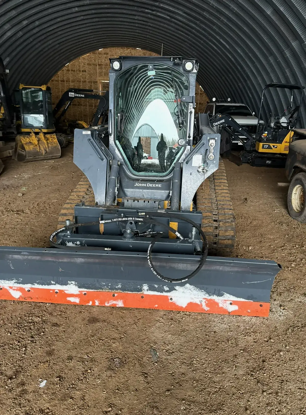 John Deere skid steer with snow plow blade parked in a shop