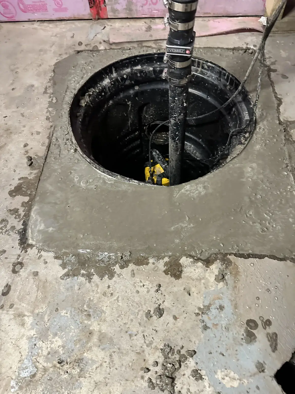New sump pit with pump and discharge pipe set in a fresh concrete basement floor