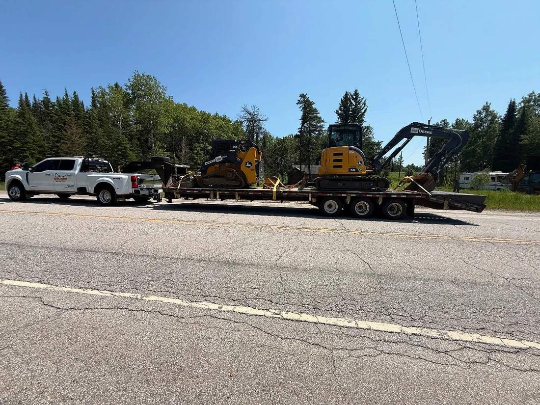 Company truck hauling two John Deere machines on a gooseneck trailer